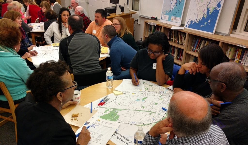 Personas reunidas alrededor de una mesa analizando mapas y tomando notas en una reunión comunitaria de planificación territorial.