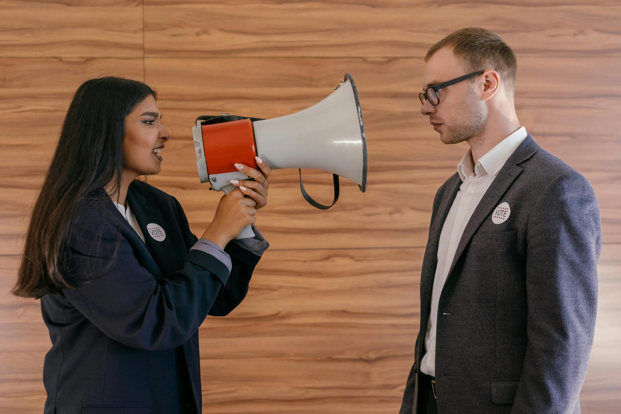 Mujer hablando con un megáfono frente a un hombre con insignia de votación, imagen que representa la exigencia de participación política y el reclamo de ser escuchados en democracia.